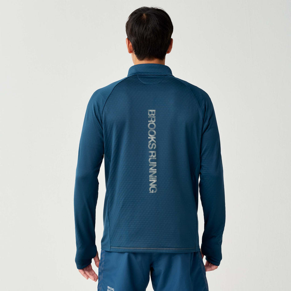 Back view of a model wearing the Brooks Men's Thermal Reflective 1/2 Zip in the Reflective Wordmark Indigo colourway.