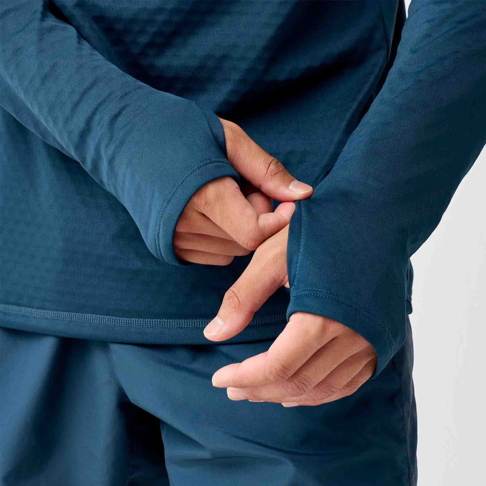 A model demonstrating the thumb loops on the Brooks Men's Thermal Reflective 1/2 Zip in the Reflective Wordmark Indigo colourway.