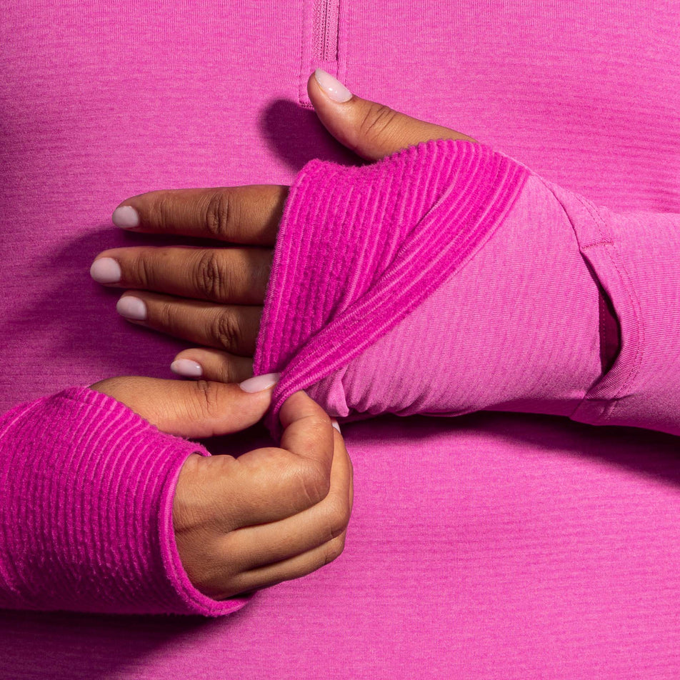 A model demonstrating that there are thumb holes in the ends of the sleeves of a Brooks Women's Notch Thermal Hoodie 2.0 in the Heather Frosted Mauve colourway. And that the fabric can be pulled over your hands. (8007496007842)