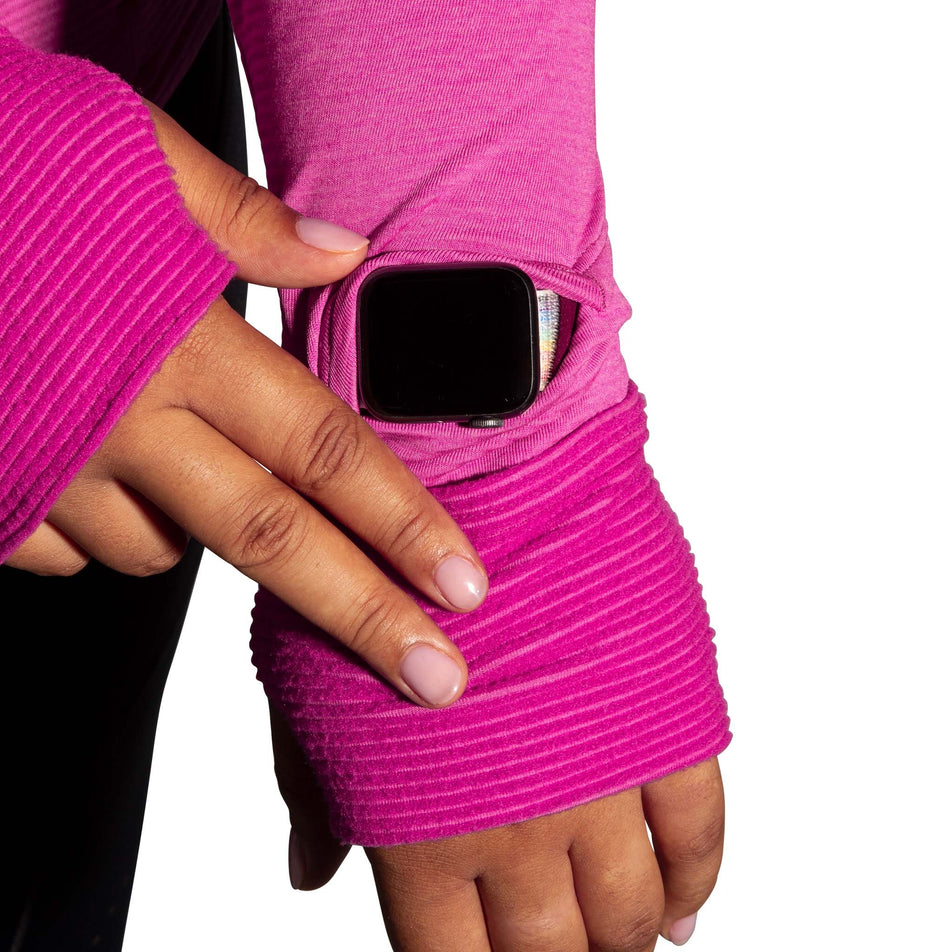A model demonstrating that there is a gap for a running watch near the cuff of the left sleeve of a Brooks Women's Notch Thermal Hoodie 2.0 in the Heather Frosted Mauve colourway. And that the fabric can be pulled over your hands. (8007496007842)