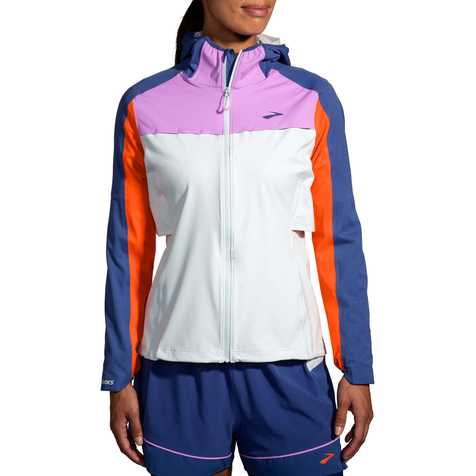 Front view of a model wearing a Brooks Women's High Point Waterproof Jacket in the Lt Slate/Bright Orange/Aegean colourway. Model is also wearing a pair of Brooks running shorts. (8037744771234)
