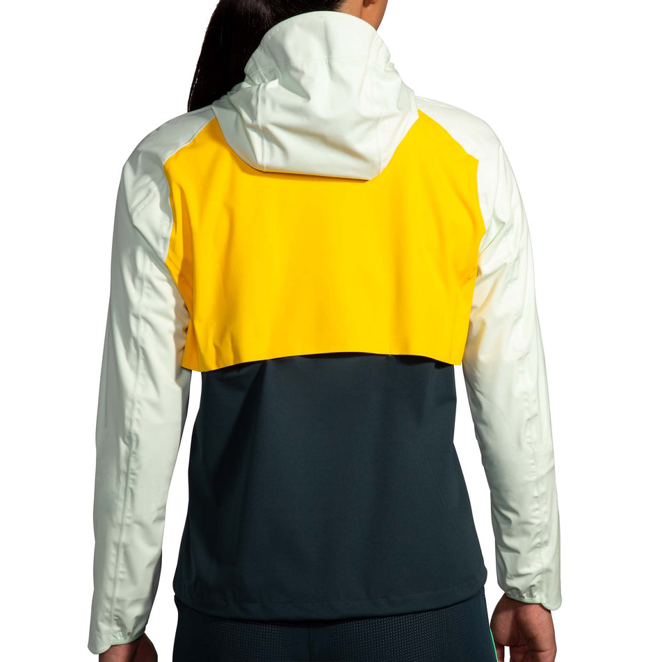 Back view of a model wearing a Brooks Women's High Point Waterproof Jacket in the Lemon/Ecru/Glacier Green colourway. Model is also wearing Brooks legwear. (8177453367458)