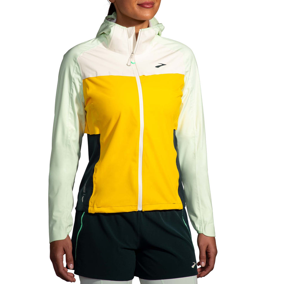 Front view of a model wearing a Brooks Women's High Point Waterproof Jacket in the Lemon/Ecru/Glacier Green colourway. Model is also wearing Brooks legwear. (8177453367458)
