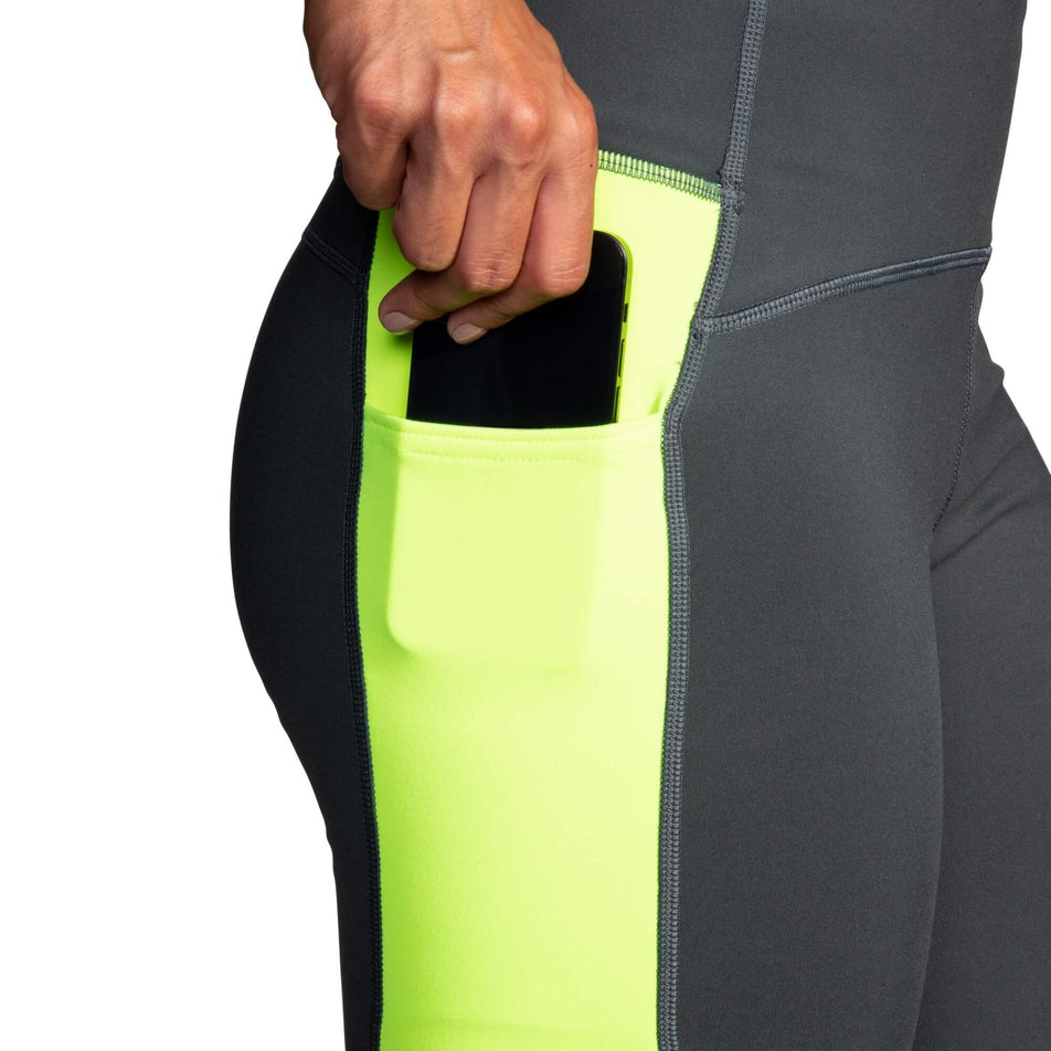 A model demonstrating that a phone can be stored in the drop-in stretch pocket on the right side of a pair of Brooks Women's Run Visible Thermal Tights (8065569194146)