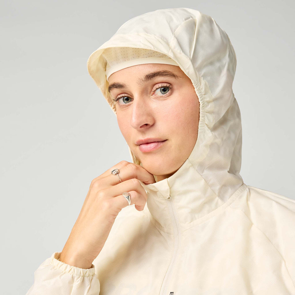 Front view of a model wearing the Brooks Women's Canopy Reflective Jacket in the Reflective Wordmark Bone colourway.