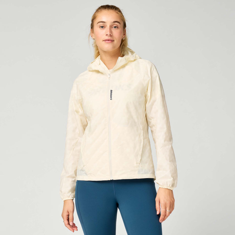 Front view of a model wearing the Brooks Women's Canopy Reflective Jacket in the Reflective Wordmark Bone colourway.
