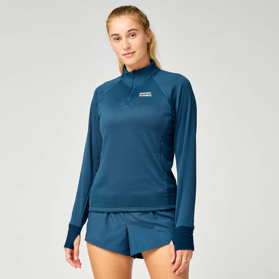 Front view of a model wearing the Brooks Women's Thermal Reflective 1/2 Zip in the Indigo/Reflective colourway.
