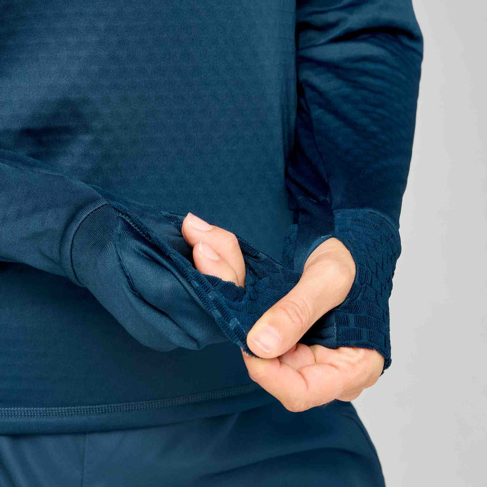 A model demonstrating the thumb loops on the Brooks Women's Thermal Reflective 1/2 Zip in the Indigo/Reflective colourway.