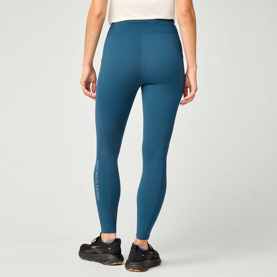 Back view of a model wearing the Brooks Women's Thermal Reflective Tight in the Indigo/Reflective colourway.