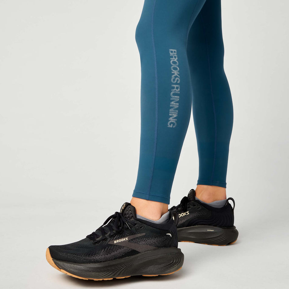 Angled view of a model wearing the Brooks Women's Thermal Reflective Tight in the Indigo/Reflective colourway.