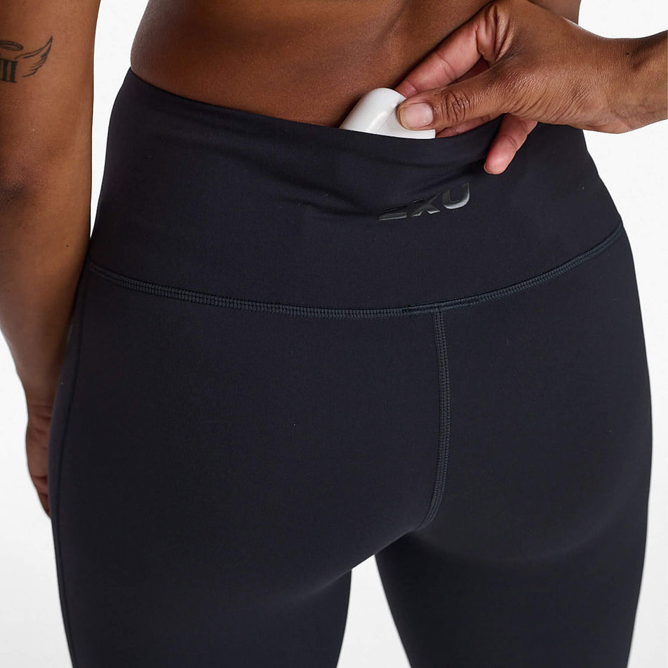 Back view of a model wearing a pair of 2XU Women's Form Hi-Rise Compression Tights in the Black/Black colourway, and demonstrating the stretch pocket on the back of the waistband.  (8248604262562)