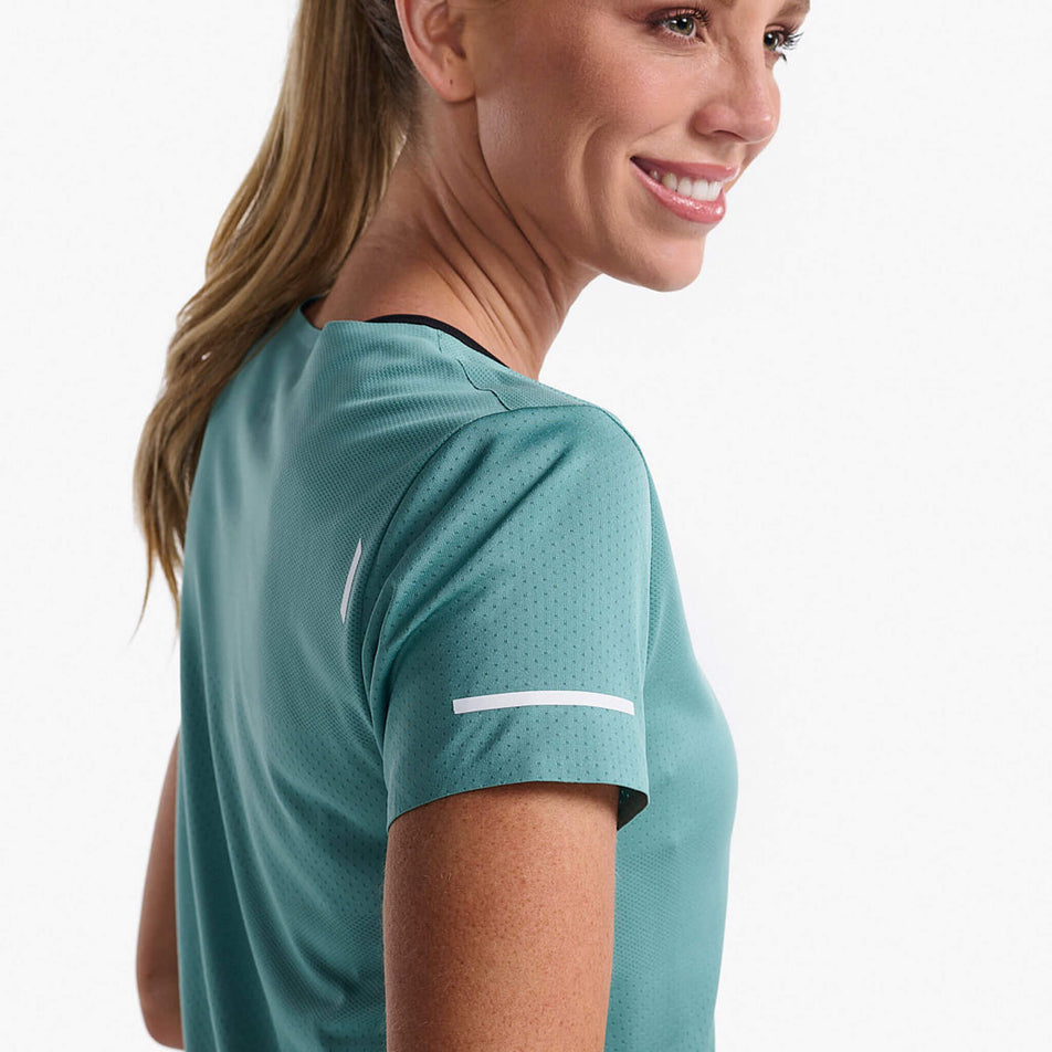 Close-up side view of a model wearing a 2XU Women's Light Speed Tech Tee in the Raft/White Reflective colourway. The upper section of the t-shirt can be seen in the image. (8250156777634)