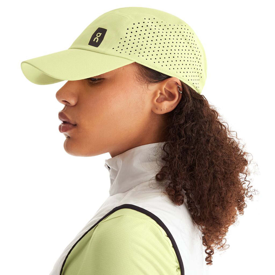 Side view of a model wearing an On Unisex Lightweight Cap in the Hay colourway. On logo is visible.  (8008510144674)