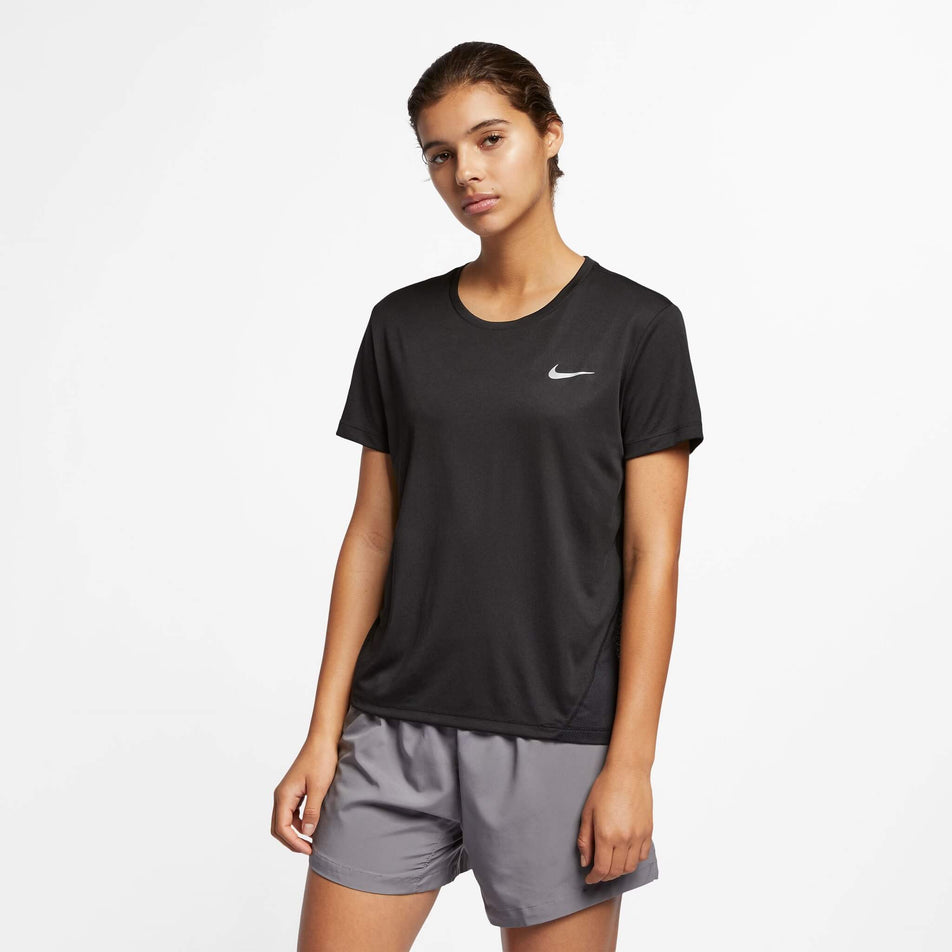 Front view of a model wearing a Nike Women's Miler Short-Sleeve Running Top in the Black/Reflective Silv colourway. Model is also wearing Nike running shorts. (8140153487522)