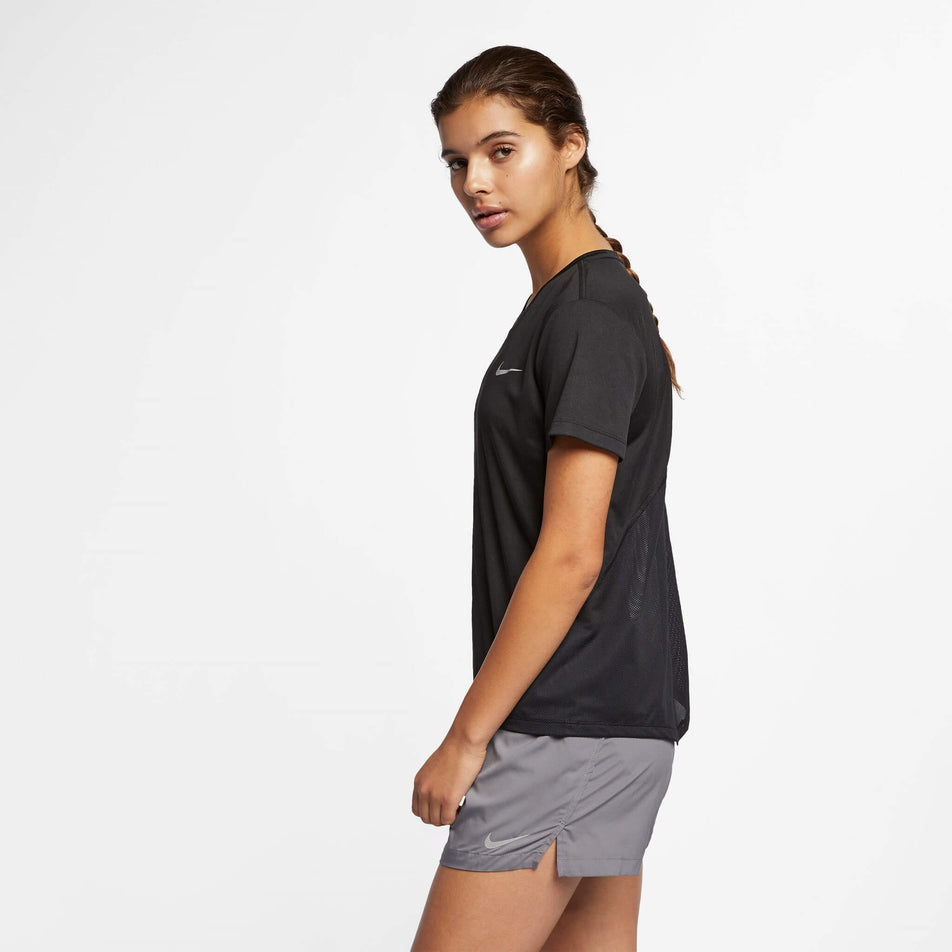 Side view of a model wearing a Nike Women's Miler Short-Sleeve Running Top in the Black/Reflective Silv colourway. Model is also wearing Nike running shorts. (8140153487522)