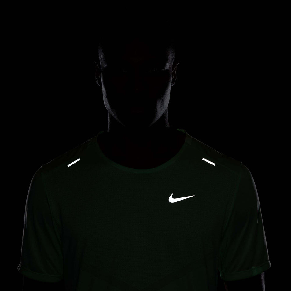 Front view of the reflective details, including the reflective Nike Swoosh, on the upper part a Nike Men's Rise 365 Dri-FIT Short-Sleeve Running Top in the Vapor Green/Reflective Silv colourway. Top is being worn by a model. (8215872766114)