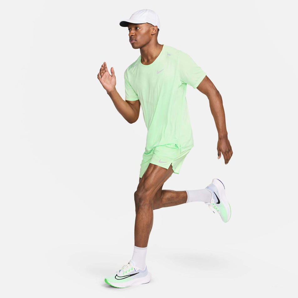 Front view of a model wearing a Nike Men's Rise 365 Dri-FIT Short-Sleeve Running Top in the Vapor Green/Reflective Silv colourway. Model is in a running pose and is also wearing Nike shorts, socks, shoes and a cap. (8215872766114)