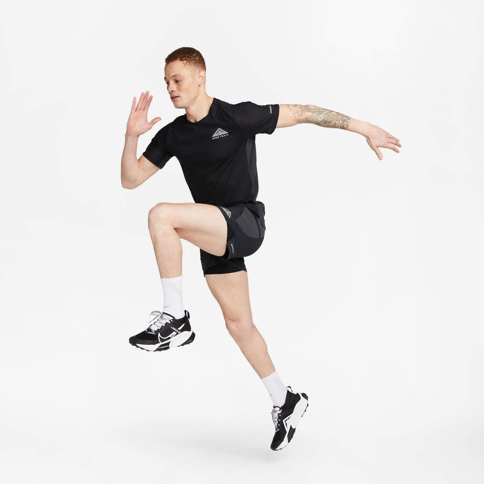 Front view of a model wearing a Nike Men's Trail Solar Chase Dri-FIT Short-Sleeve Running Top in the Black/White colourway. Model is in a running pose, and also wearing a pair of Nike shorts, socks and shoes. (8140170199202)