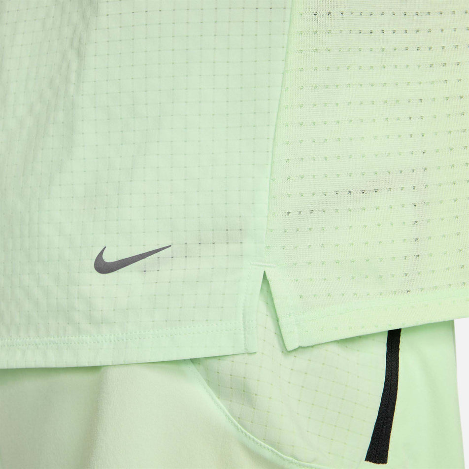 Close-up left side view of the stitching detail at the bottom of a Nike Men's Trail Solar Chase Dri-FIT Short-Sleeve Running Top in the Vapor Green/Black colourway.  (8215882825890)