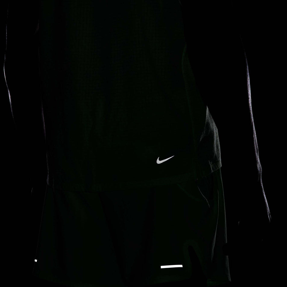 Close-up view of the reflectivity provided by the Nike Swoosh logo on the lower back right side of a Nike Men's Trail Solar Chase Dri-FIT Short-Sleeve Running Top in the Vapor Green/Black colourway. (8215882825890)