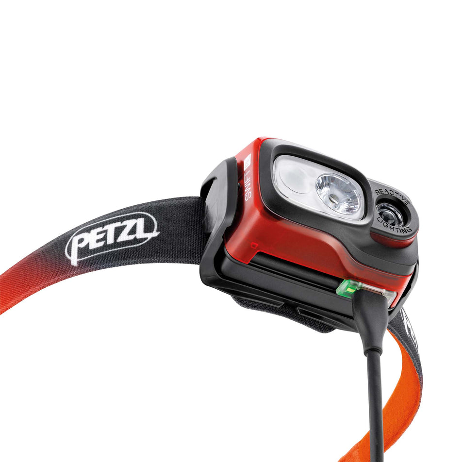 Underside front view of a Petzl SWIFT RL Head Torch in the Orange colourway, with a charging cable attached. (8065363247266)