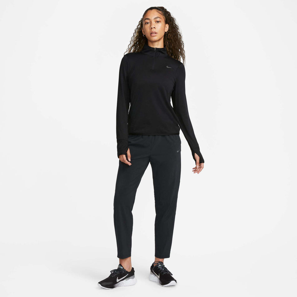 Front view of a model wearing a Nike Women's Dri-FIT Swift Element UV 1/4-Zip Running Top in the Black/Reflective Silv colourway. Model is also wearing Nike trousers and Nike shoes. (8049594007714)