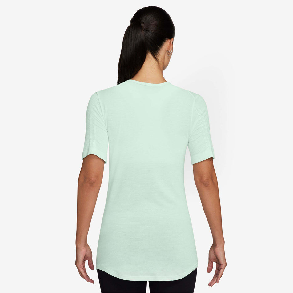 Back view of a model wearing a Nike Women's Swift Wool Dri-FIT Short-Sleeve Running Top in the Barely Green colourway. Model is also wearing black leggings. (8215861428386)