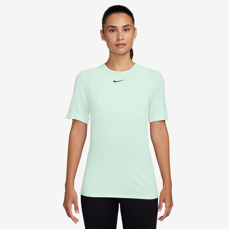 Front view of a model wearing a Nike Women's Swift Wool Dri-FIT Short-Sleeve Running Top in the Barely Green colourway. Model is also wearing black leggings.  (8215861428386)