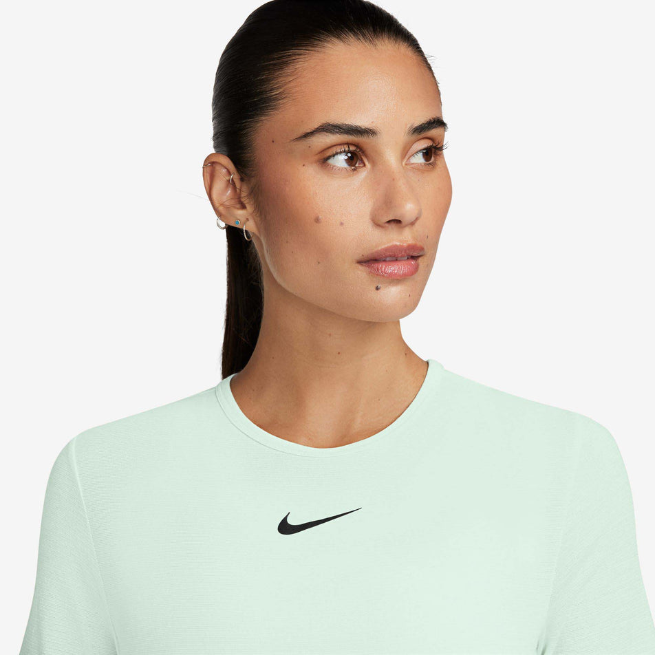 Close-up front view of a model wearing a Nike Women's Swift Wool Dri-FIT Short-Sleeve Running Top in the Barely Green colourway. The upper third of the top is visible in the image. (8215861428386)