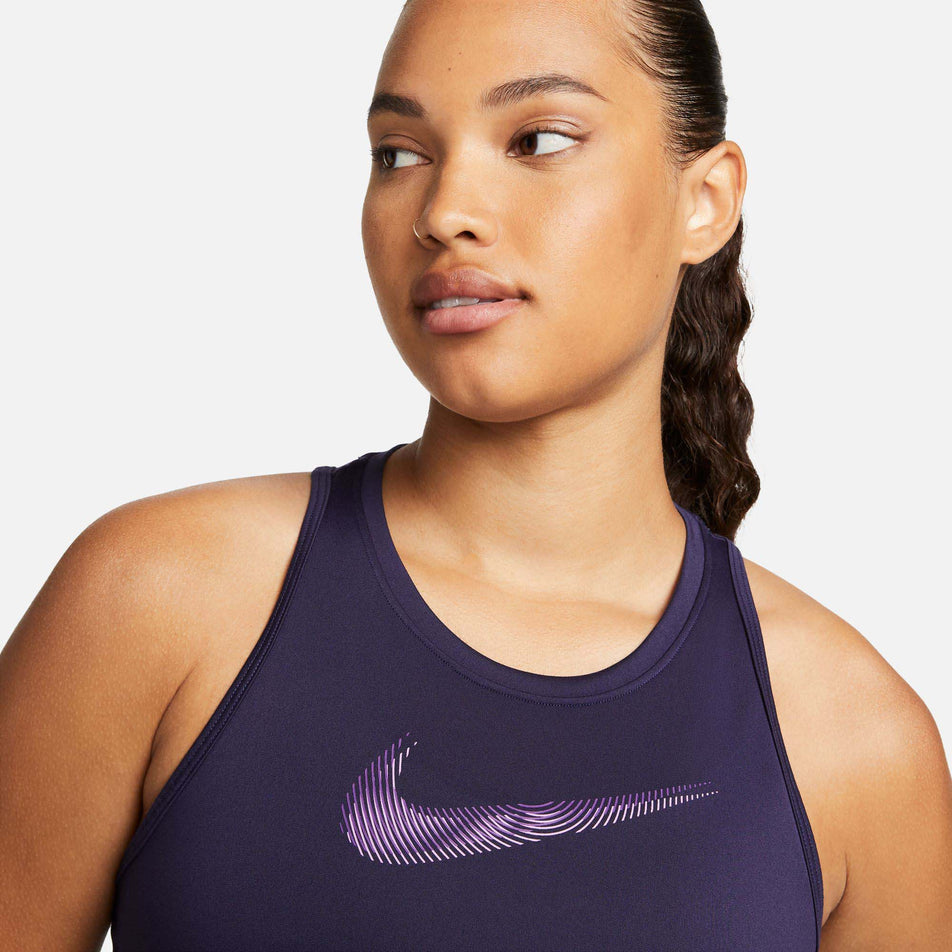 Close-up front view of a model wearing a Nike Women's Dri-FIT Swoosh Tank Top in the Purple Ink/Disco Purple colourway. Upper section of the tank top is in view. (7980177719458)