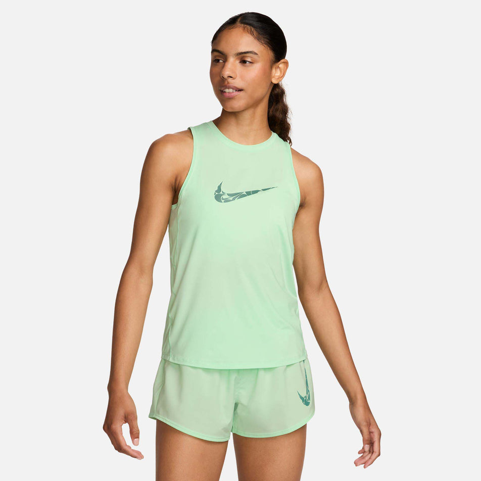 Front view of a model wearing a Nike Women's One Graphic Running Tank Top in the Vapor Green/Bicoastal colourway. Model is also wearing Nike shorts. (8299396104354)