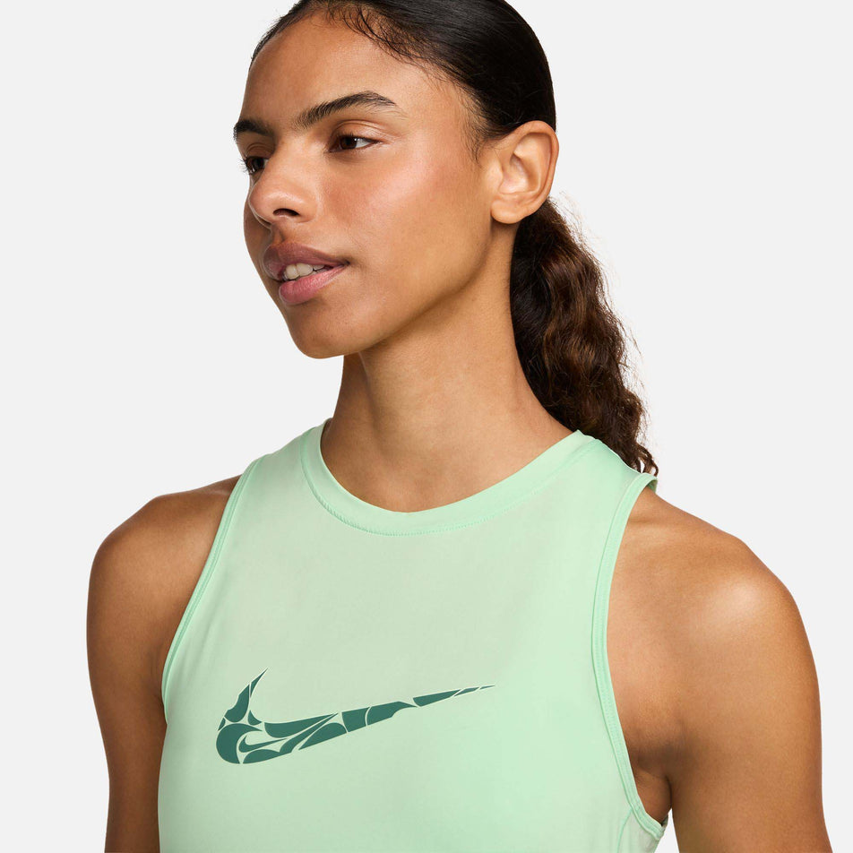 Close-up view of the upper front section of a Nike Women's One Graphic Running Tank Top in the Vapor Green/Bicoastal colourway. Top is being worn by a model. (8299396104354)
