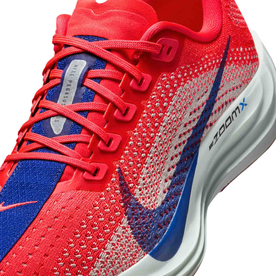 Close up of the upper of the left shoe from a pair of Nike Women's Pegasus Plus Road Running Shoes in the Bright Crimson/Deep Royal Blue-Silt colourway. (8686778581154)