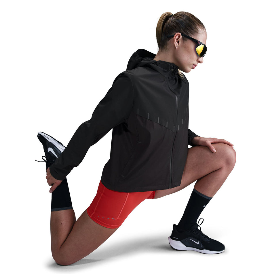 Side view of a model wearing the Nike Women's AeroSwift Aerogami Storm-FIT Running Jacket in the Black/Black colourway.