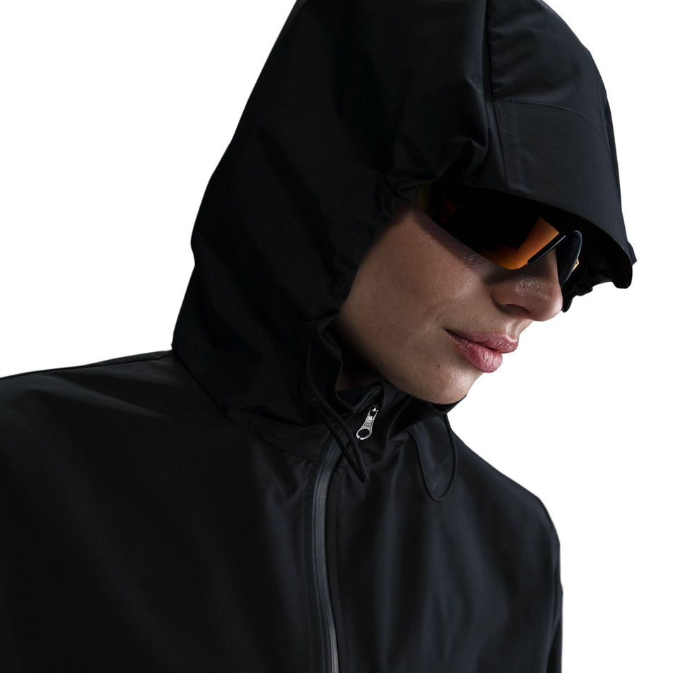 Front view of a model wearing the Nike Women's AeroSwift Aerogami Storm-FIT Running Jacket in the Black/Black colourway with the hood up.