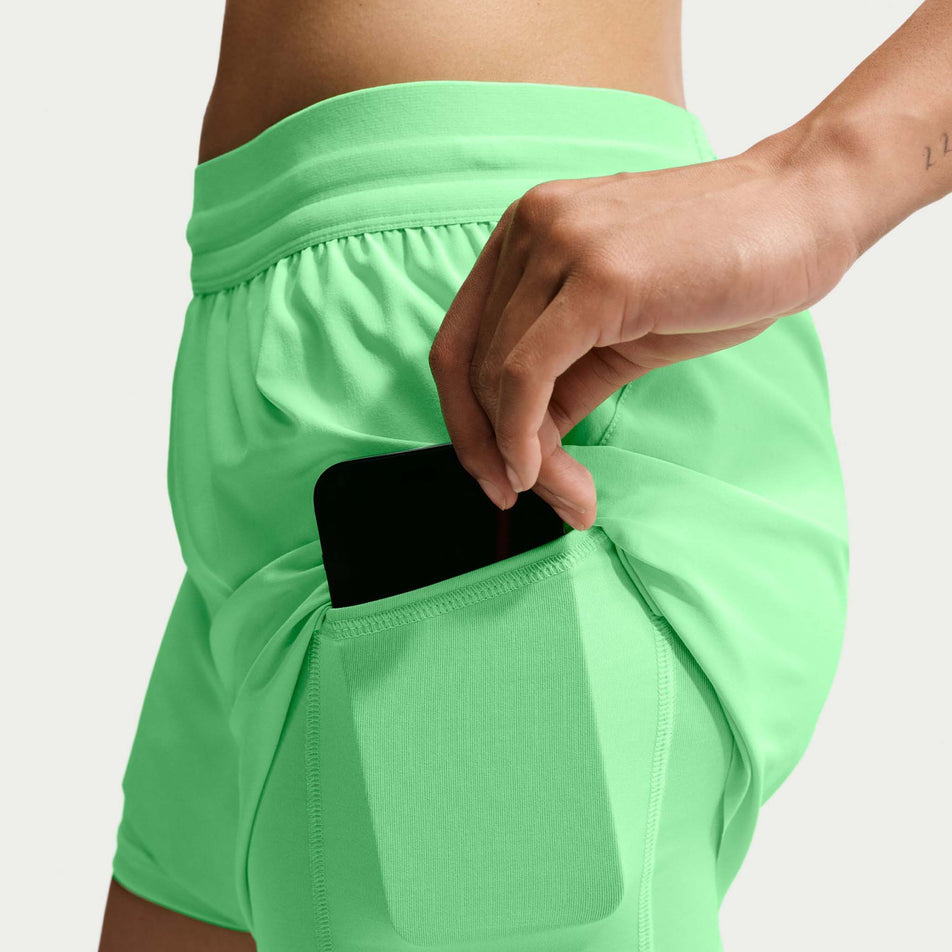 A model demonstrating the stash pocket on the the Nike Women's Swift Dri-FIT Mid-Rise 2-in-1 Running Shorts in the Illusion Green colourway.