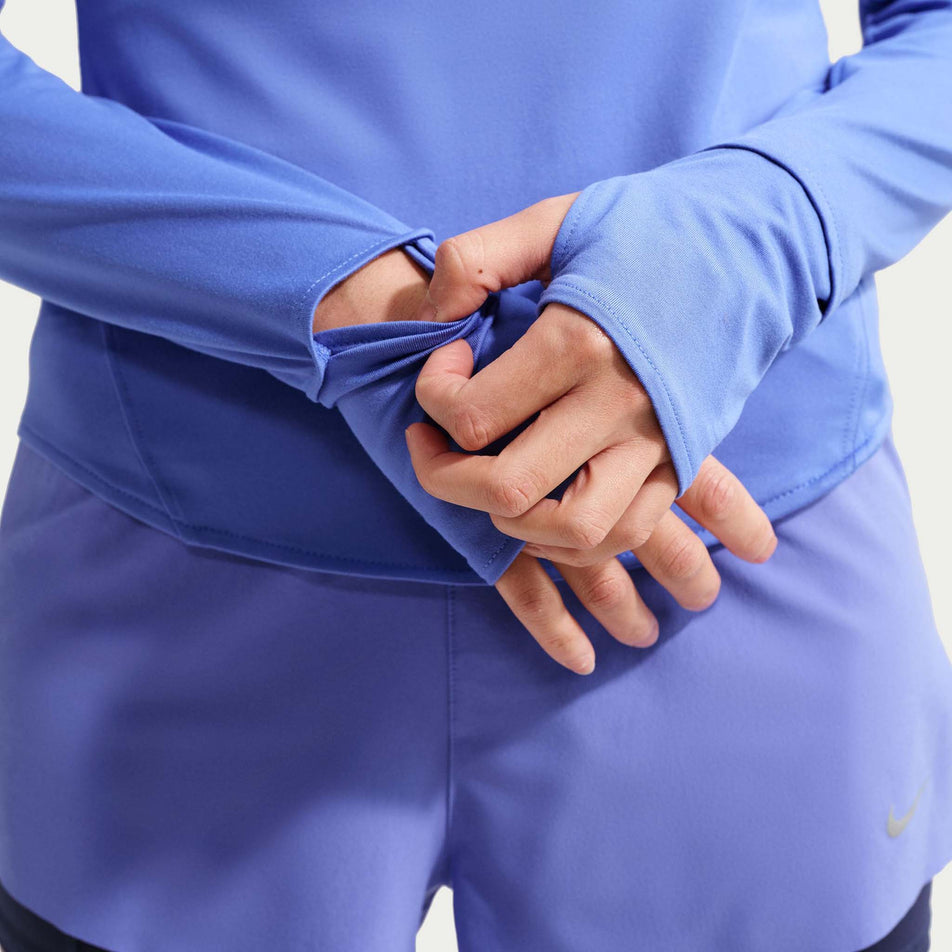 A model demonstrating the watch window on the Nike Women's Swift Dri-FIT UV 1/4-Zip Running Top in the Sapphire/Reflective Silver colourway.
