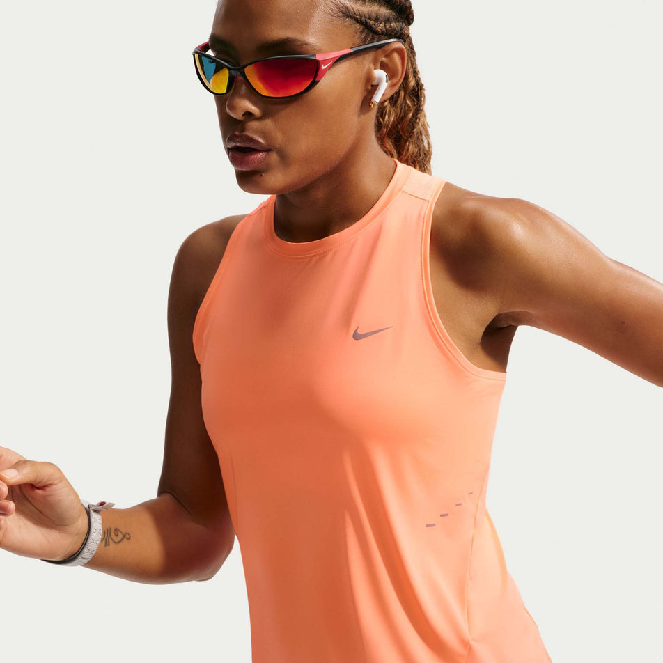 Angled view of a model wearing the Nike Women's Swift Dri-FIT Running Tank Top in the Orange Pulse/Reflective Silver colourway.