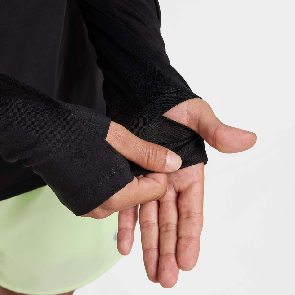 A model demonstrating the thumbloops on the sleeves of the Nike Men's Stride Dri-FIT 1/4-Zip Running Top in the Black/Reflective Silver colourway. (8778198876322)