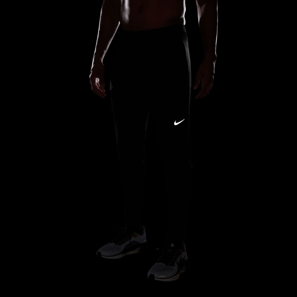 The reflective Swoosh logo on the front of the Nike Men's Dri-FIT Stride Knit Running Pants in the Black/Reflective Silver colourway. (8733229744290)