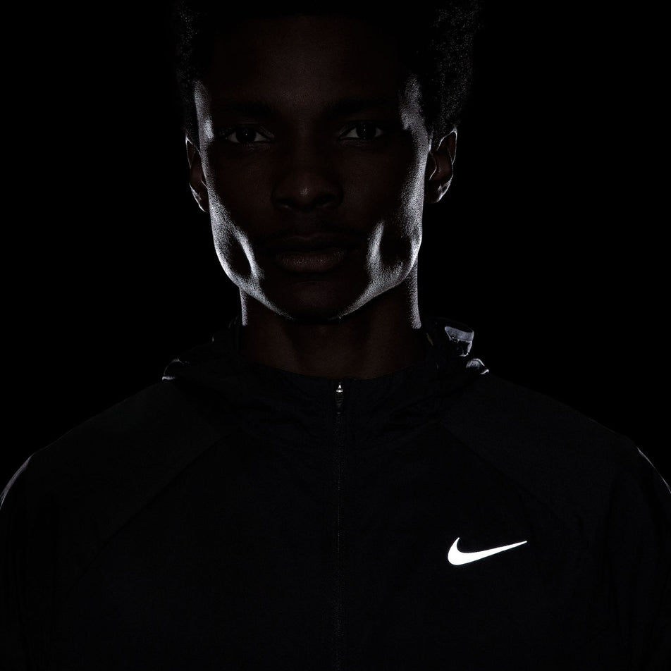 The reflective Nike Swoosh logo on the front of the Nike Men's Stride Repel UV Running Jacket in the Black/Black/Reflective Silver colourway.