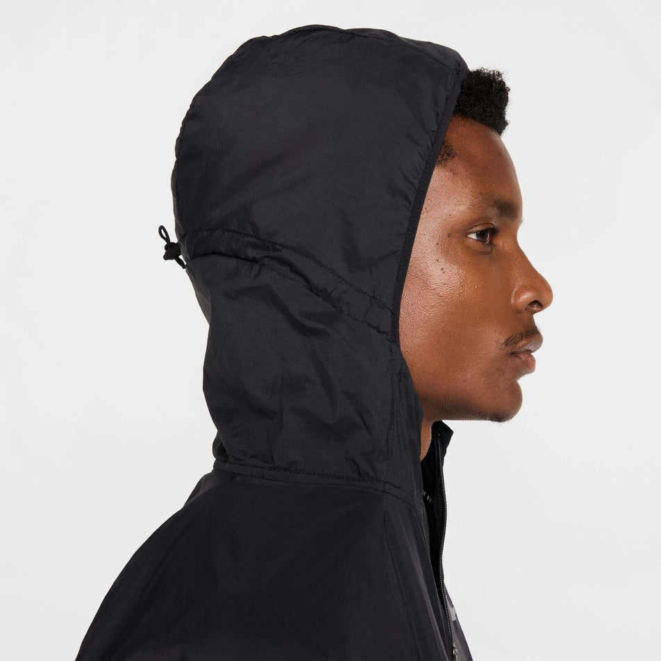 Side view of a model wearing the Nike Men's Stride Repel UV Running Jacket in the Black/Black/Reflective Silver colourway with the hood up.