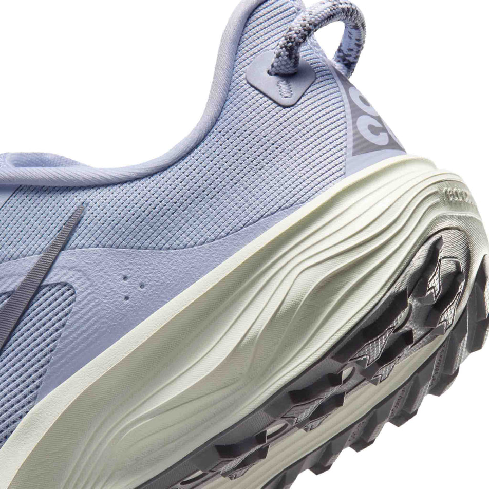 Close-up view of the rearfoot section of the left shoe from a pair of Nike Women's ACG Pegasus Trail Running Shoes in the Ghost/Cement Grey-Mineral Slate colourway.