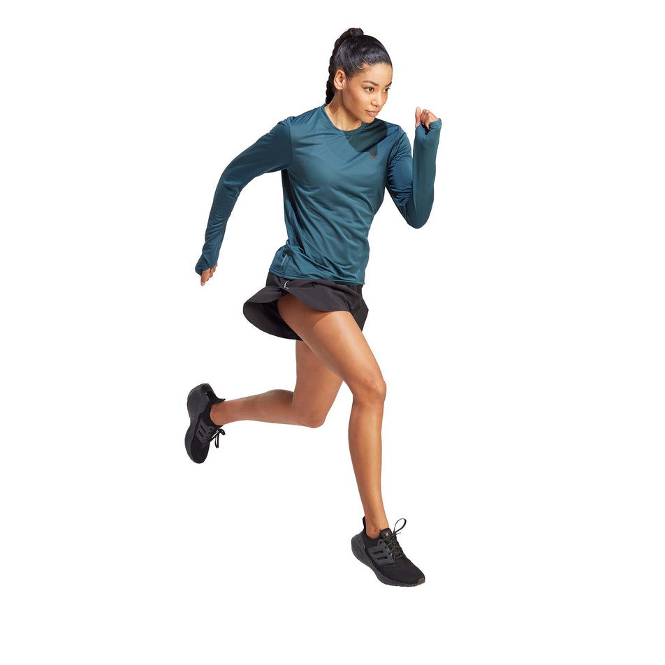Angled front view of a model wearing an adidas Women's Run Icons Running Long-Sleeve Top in the Arctic Night colourway. Model is in a running pose.  (8005336432802)