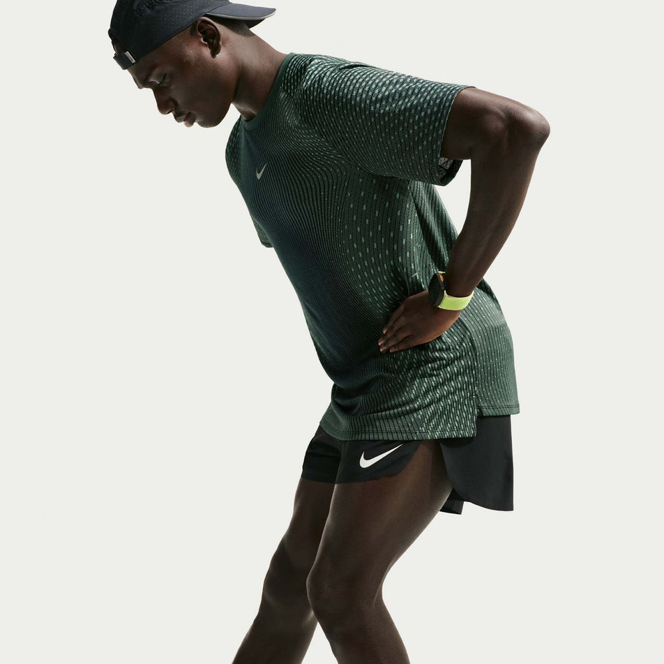 Angled view of a model wearing the Nike Men's Stride Aero-FIT Short-Sleeve Running Top in the Black/Light Green Spark/Reflective Silver colourway.