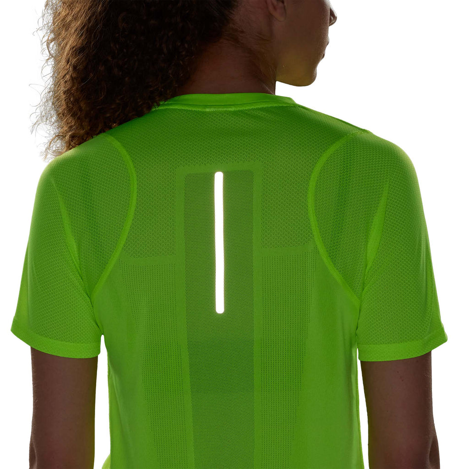 Close-up back view of a model wearing an adidas Women's Ultimate Knit T-Shirt in the Lucid Lemon colourway. Upper two-thirds of the top is visible in low light conditions to show the reflective strip on the back. (8005345771682)