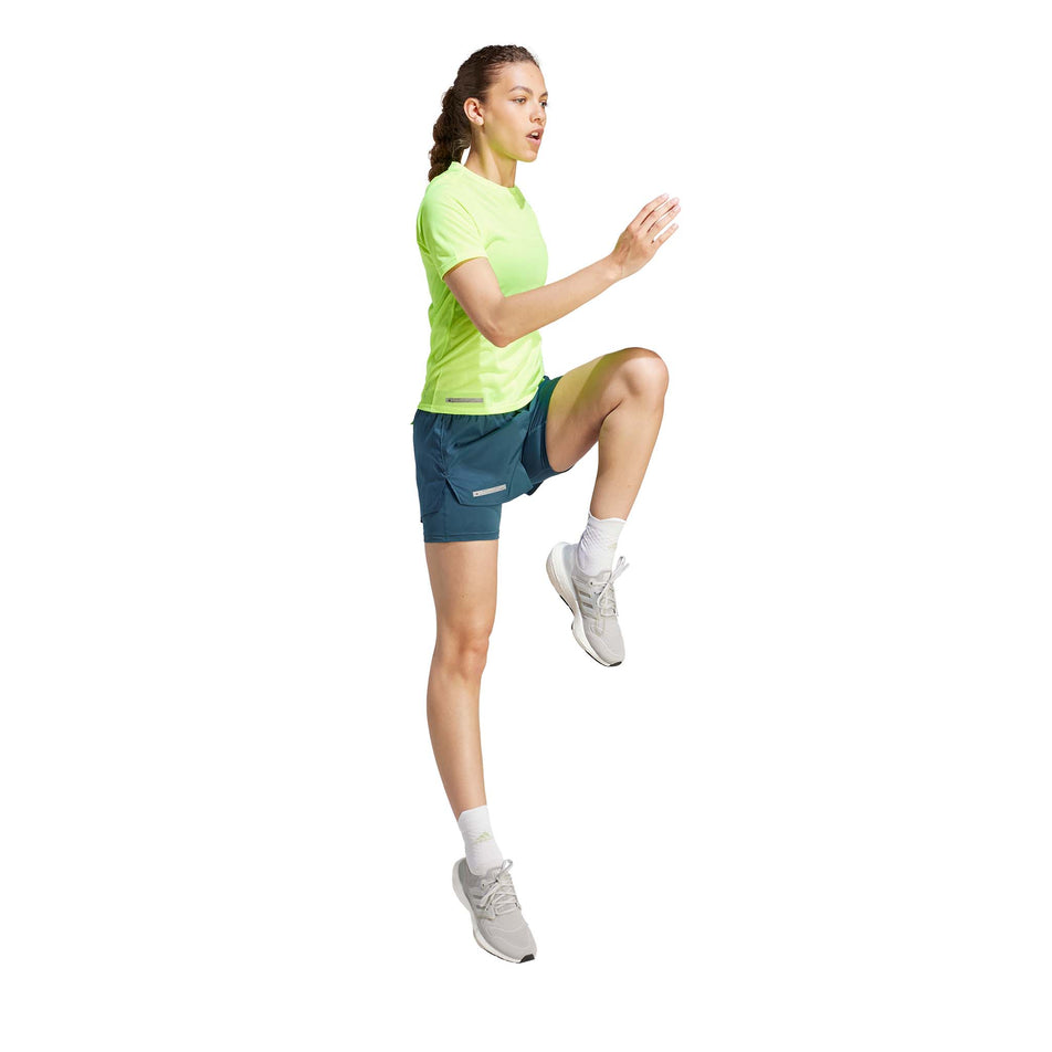 Side view of a model wearing an adidas Women's Ultimate Knit T-Shirt in the Lucid Lemon colourway. Model is in a running pose.  (8005345771682)