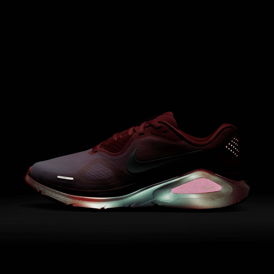 The reflective detail on the lateral side of the left shoe from a pair of Nike Women's Structure 26 Road Running Shoes in the Light Redwood/Barely Green-Team Red colourway.