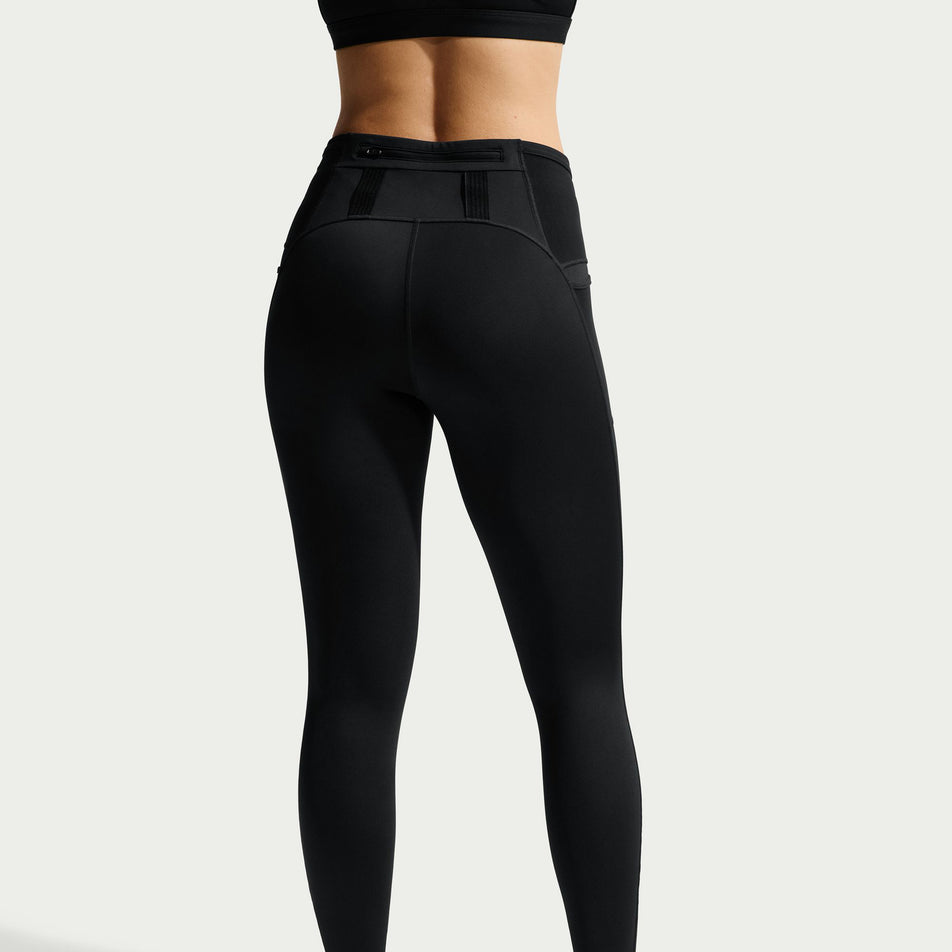 Back view of a model wearing the Nike Women's ACG Dri-FIT High-Waisted 7/8 Trail Running Leggings in the Black/Summit White colourway.