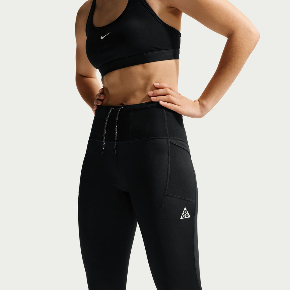 Angled view of a model wearing the Nike Women's ACG Dri-FIT High-Waisted 7/8 Trail Running Leggings in the Black/Summit White colourway.